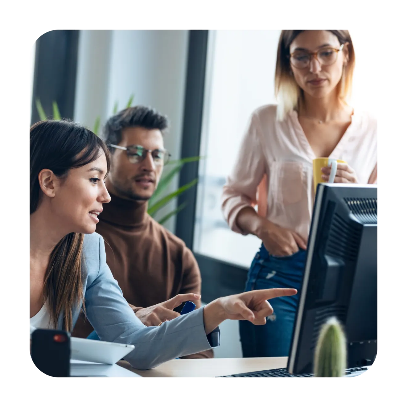 Three colleagues around a monitor, one of them pointing at the screen
