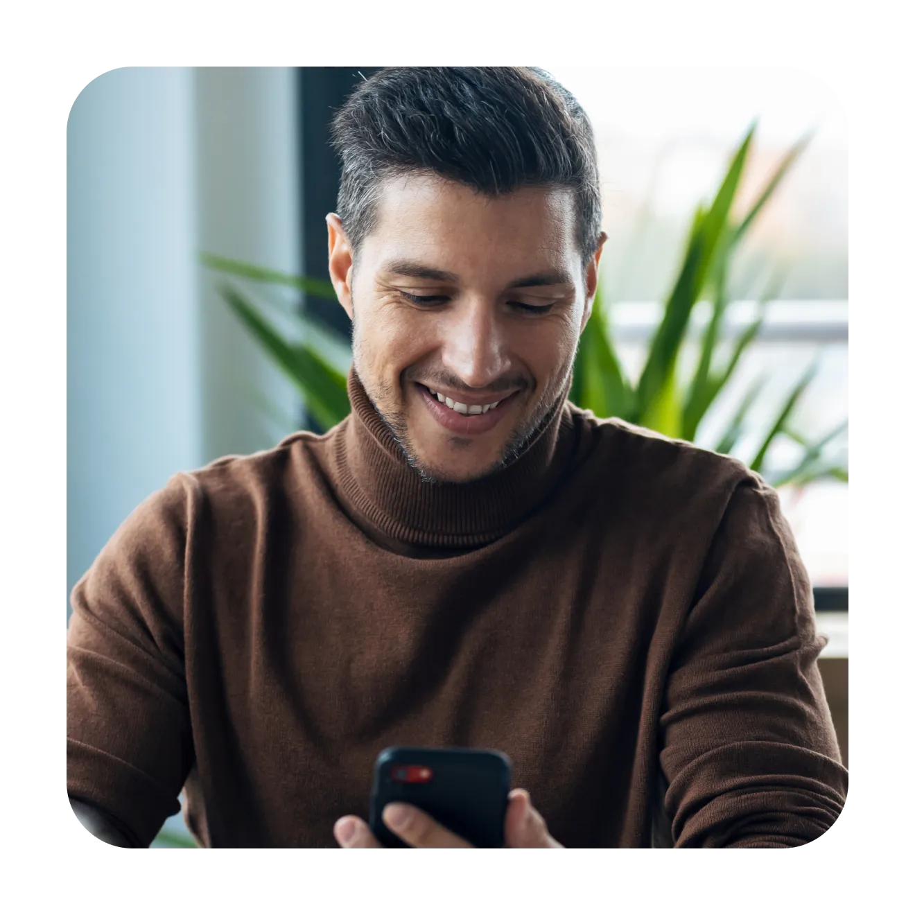 Man in a brown turtleneck smiling at his phone